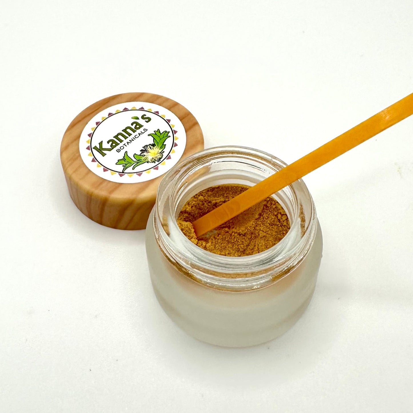 Small opaque glass 1g jar with clear top edge containing tannish orange Kanna Full Spectrum Extract Powder in front of a wooden lid with Kanna's Botanicals logo sticker on top. An small plastic orange scoop placed in the kanna powder.
Product: Kanna Full Spectrum Extract Powder(1g jar). 
- Kanna's Botanicals LLC